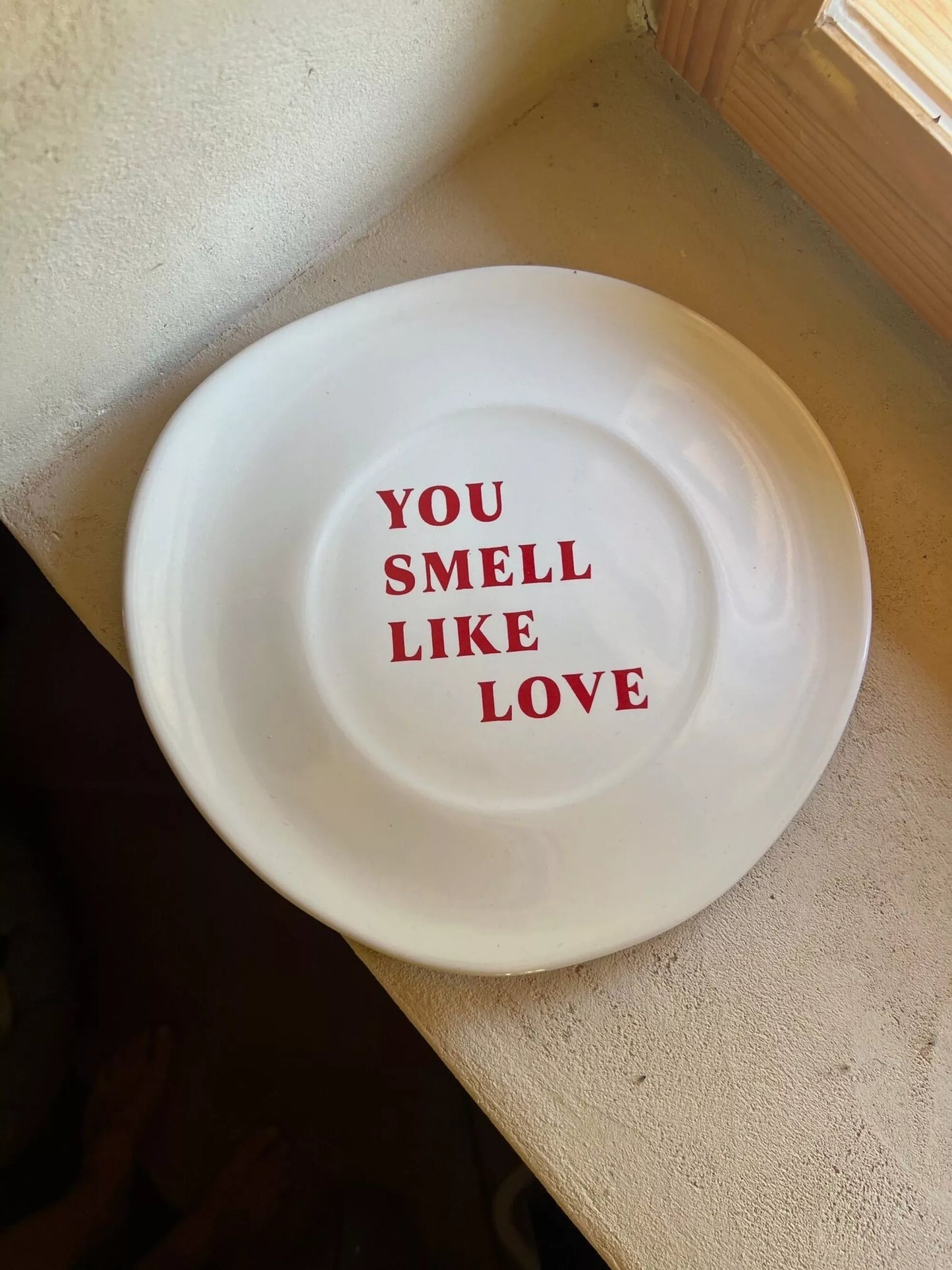 Assiette Tu sens l'amour blanche cassée avec texte rouge « You smell like love », finition brillante, idéale pour dessert ou décoration murale.