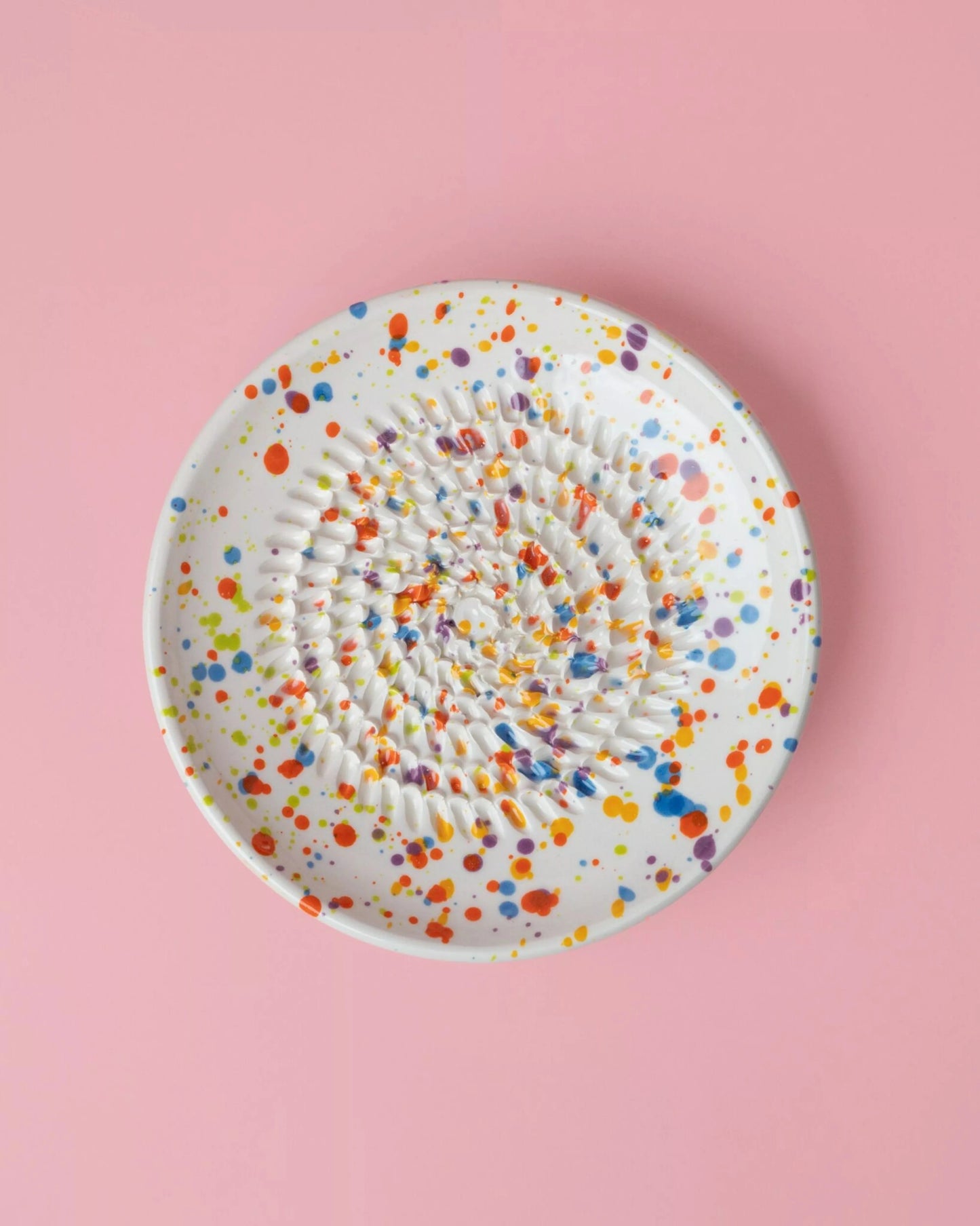 Râpe en céramique multicouleur compacte pour ail et gingembre, design éclaboussé coloré sur fond rose. Ustensile de cuisine facile à nettoyer.