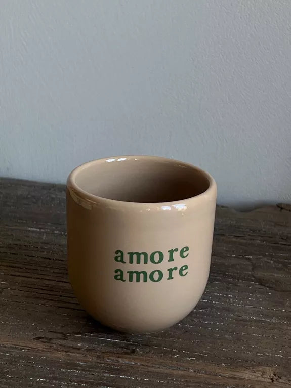 Mug Amore Amore beige en céramique artisanale avec lettrage vert, posé sur une table en bois rustique. Parfait pour un usage quotidien au petit-déjeuner.