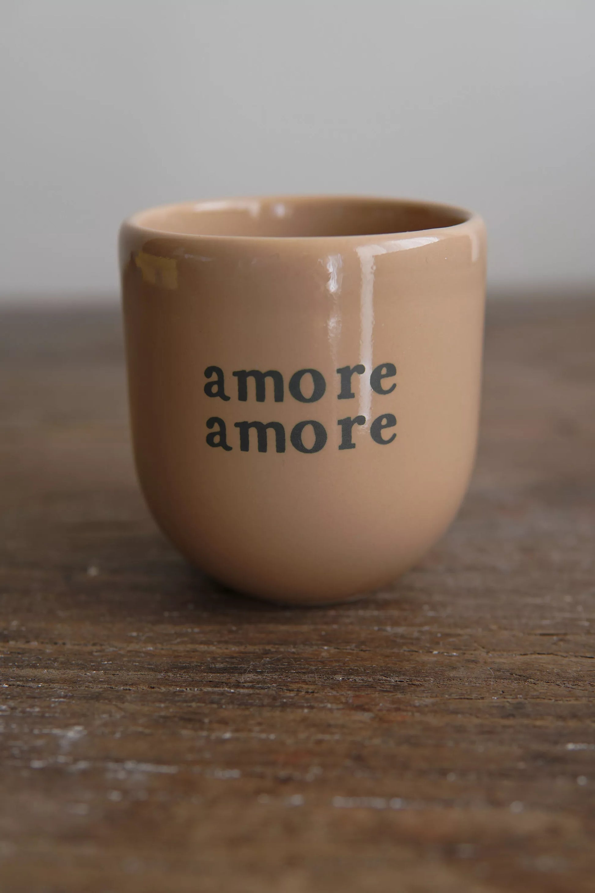 Mug Amore Amore beige en céramique artisanale avec lettrage vert, posé sur une table en bois rustique. Parfait pour un usage quotidien au petit-déjeuner.