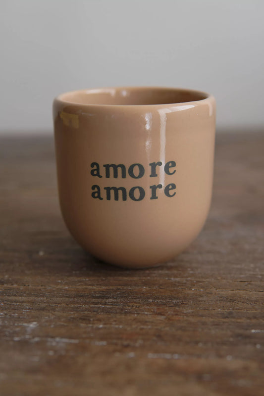 Mug Amore Amore beige en céramique artisanale avec lettrage vert, posé sur une table en bois rustique. Parfait pour un usage quotidien au petit-déjeuner.