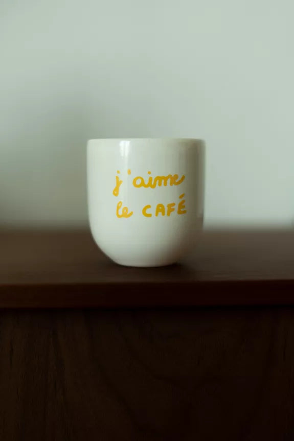 Mug J'aime le café en céramique blanche avec lettrage jaune, posé sur une étagère en bois. Tasse artisanale de 20cl pour amateurs de café.